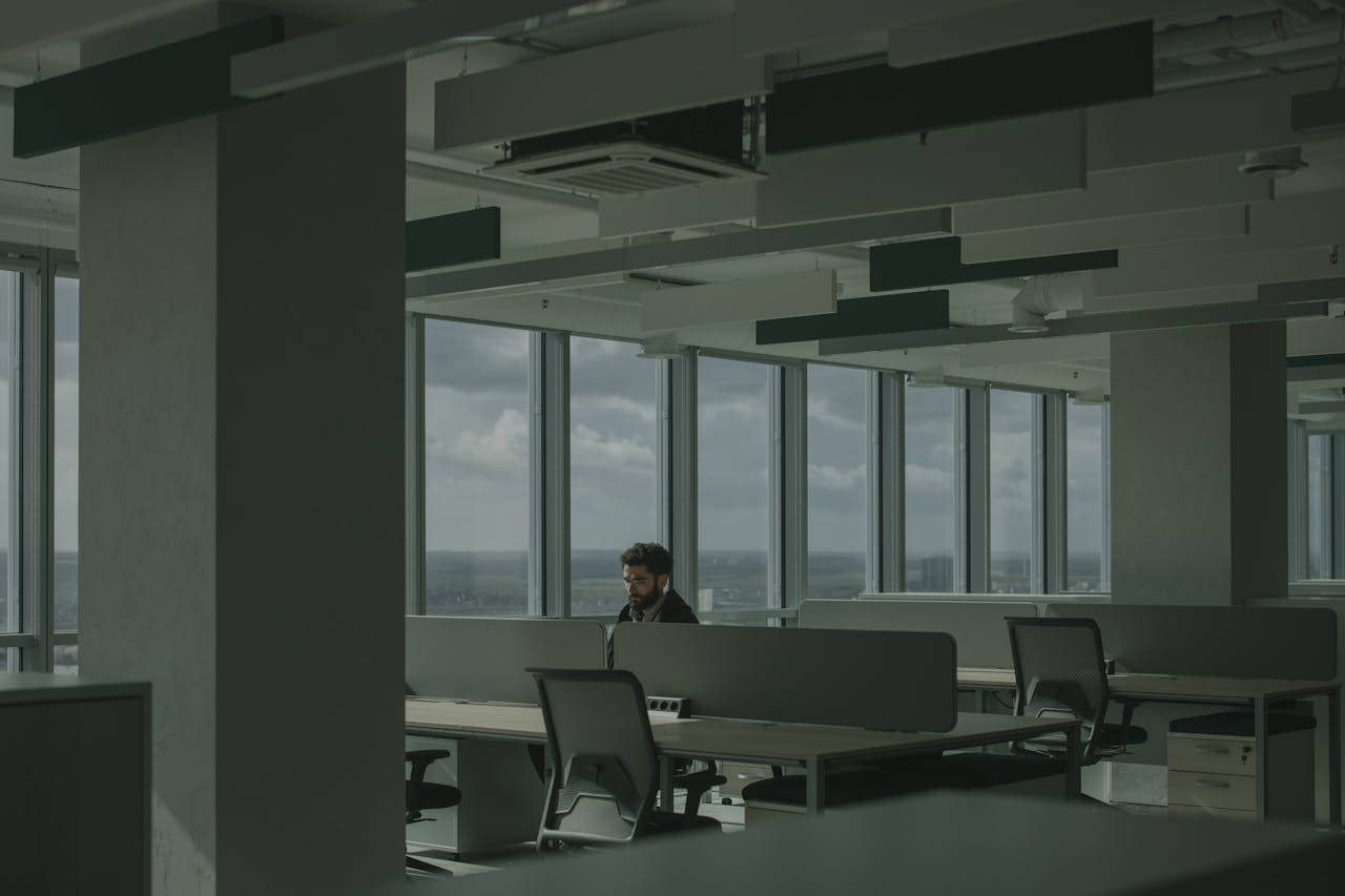 A man works alone in a spacious, modern office with large windows and natural light.