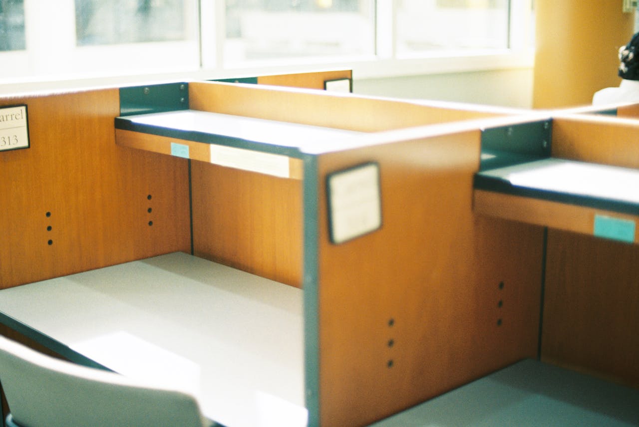 Empty wooden cubicles in a sunlit office space, offering a modern professional ambience.